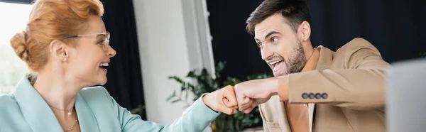 Молодой возбужденный менеджер делает удар кулаком с улыбающейся бизнесвумен в очках в офисе, баннер — стоковое фото