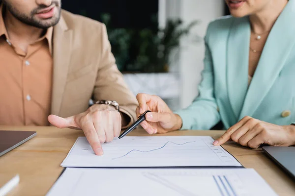 Cropped view of business partners pointing at graphs while working with papers in office — Stock Photo