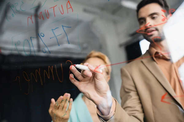 Verschwommener Geschäftsmann mit Filzstift auf Klemmbrett neben Frau, die mit Hand im Büro zeigt — Stockfoto