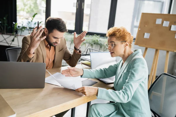 Displeased businesswoman pointing at document while talking to shocked manager in office — Stock Photo
