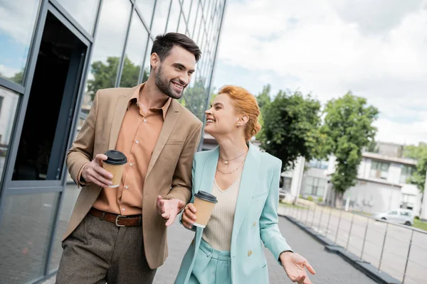 Compañeros de negocios alegres y exitosos caminando con café para salir a la calle urbana - foto de stock