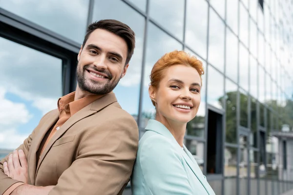 Overjoyed business colleagues in trendy blazers looking at camera near glass building on urban street — Stock Photo