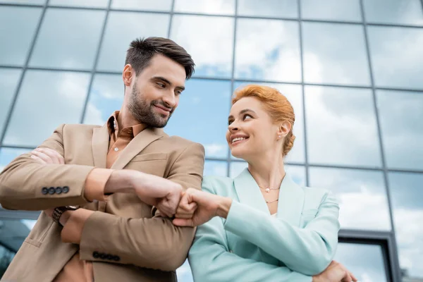 Low angle view of successful business partners looking at each other and doing fist bump on urban street — Stock Photo