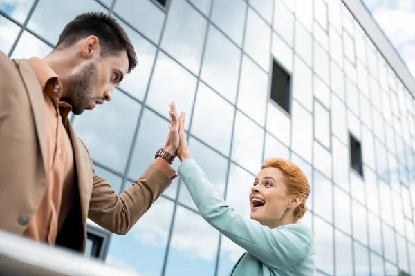 Low angle view of excited business colleagues giving high five near modern building on city street — Stock Photo