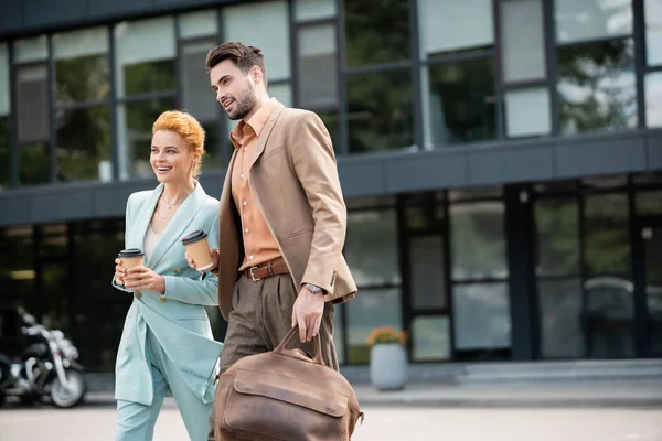 Successful and stylish business partners with paper cups walking on city street — Stock Photo