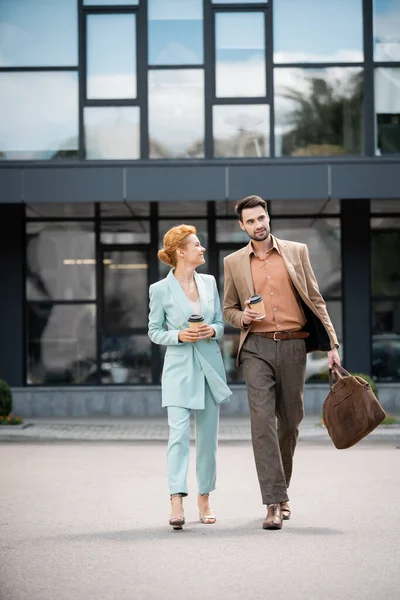 Piena lunghezza di donna d'affari felice con caffè per andare a parlare con il partner d'affari sorridente mentre cammina sulla strada della città — Foto stock