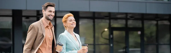 Happy business partners with takeaway drinks looking away and smiling on urban street, banner — Stock Photo