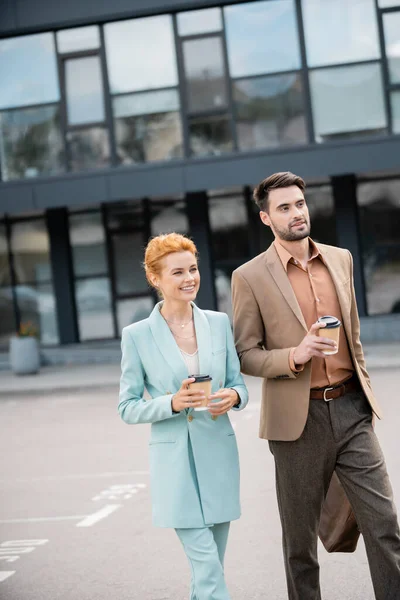 Joyful business colleagues in stylish blazers holding coffee to go and smiling on street in city — Stock Photo
