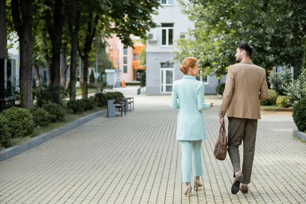 Rückansicht stilvoller Geschäftskollegen, die sich beim Spaziergang durch die grüne Gasse in der Stadt unterhalten — Stockfoto