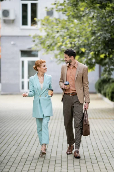 Full length of joyful businesswoman talking to colleague while walking on urban street — Stock Photo