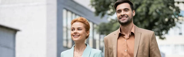 Happy business partners in trendy blazers looking away on blurred city street, banner — Stock Photo