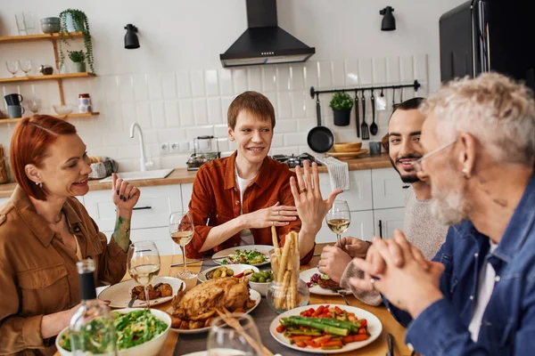 Feliz gay hombre mostrando boda anillo a padres durante familia cena en cocina - foto de stock