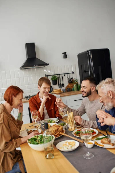 Happy gay man holding hand of boyfriend while showing wedding ring to parents during family supper — Stock Photo