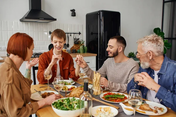 Bearded gay man holding hand of redhead boyfriend and showing wedding ring to parents during supper in kitchen — Stock Photo