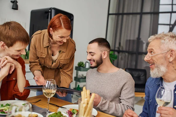 Cheerful gay couple looking at photo album during supper with happy family at home — Stock Photo
