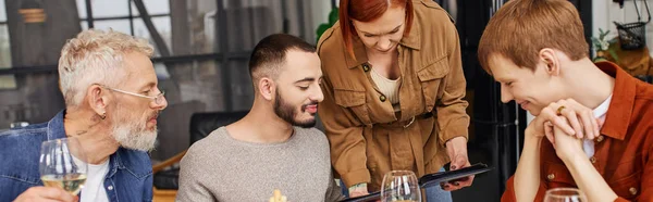 Бородатий чоловік і молода пара гей дивиться на фотоальбом під час сімейної вечері у вітальні, банер — стокове фото