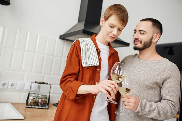 Bearded gay man clinking wine glasses with smiling redhead boyfriend kitchen — Stock Photo