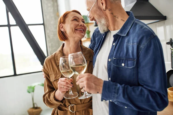 Stilvolles und fröhliches Paar, das in der Küche Weingläser klimpert und einander anlächelt — Stockfoto