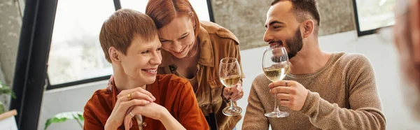 Barbuto gay uomo brindare con vino vicino felice fidanzato e rossa donna in cucina, striscione — Foto stock
