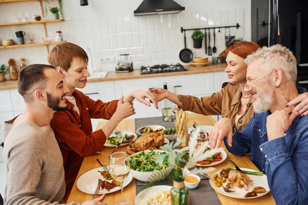 Sorrindo gay homem mostrando casamento anel para mãe perto namorado e família jantar no cozinha — Fotografia de Stock