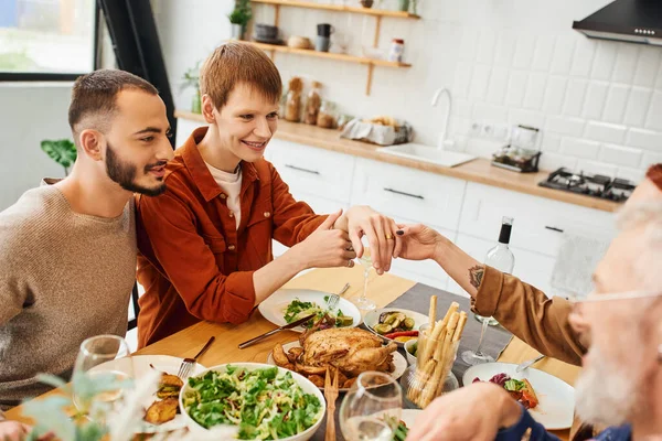 Contento gay uomo mostrando matrimonio anello durante famiglia cena con fidanzato e genitori in cucina — Foto stock