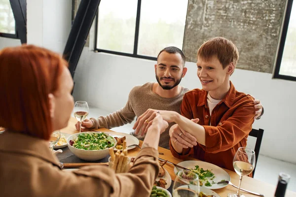 Happy gay man showing wedding ring to mother near boyfriend and delicious supper served in kitchen — Stock Photo