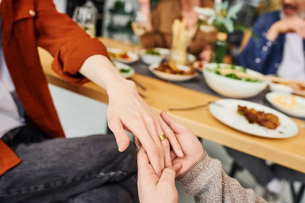 Corte vista de gay homem segurando mão no namorado no casamento anel perto borrado ceia e pais em casa — Fotografia de Stock