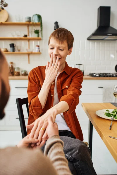 Amazed gay man covering mouth with hand near blurred boyfriend making marriage proposal in kitchen — Stock Photo