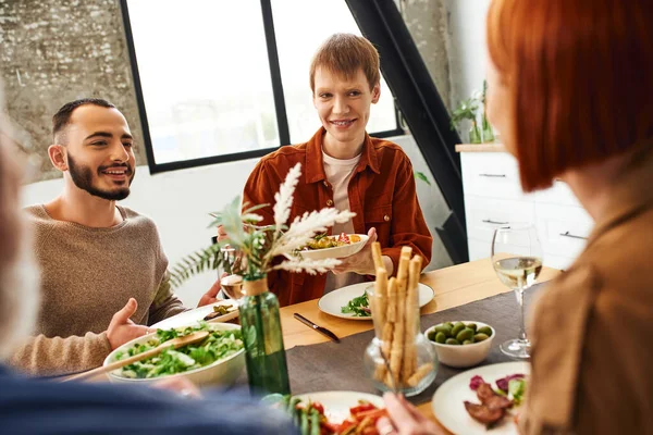 Happy gay couple talking to blurred parents during family supper at home — Stock Photo