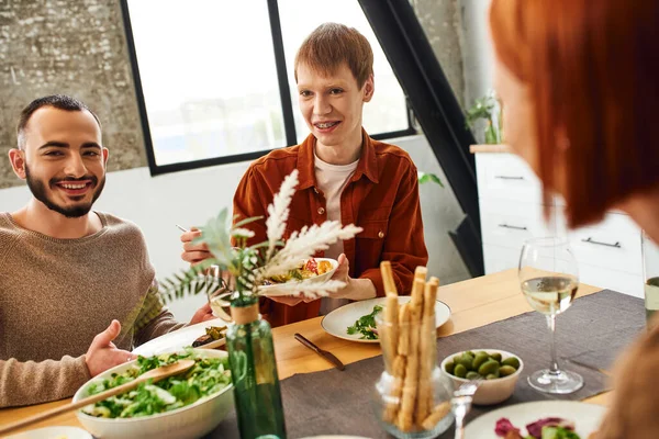 Positive gay man smiling near boyfriend and mother next to delicious supper in kitchen — Stock Photo