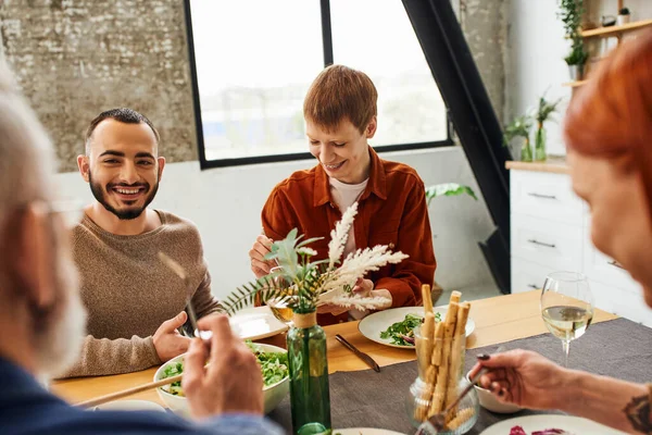 Smiling bearded gay man talking during family supper with boyfriend and parents at home — Stock Photo