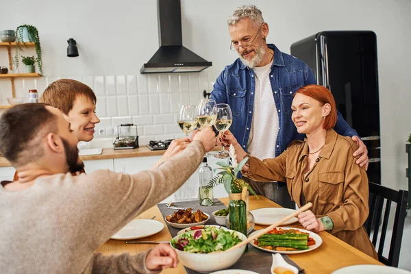 Giovane coppia gay clinking bicchieri di vino con i genitori vicino cena servita in cucina moderna — Foto stock