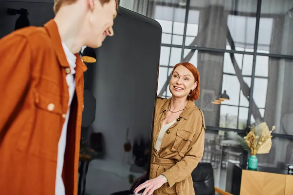 Happy redhead woman looking at blurred son near fridge in modern kitchen — Stock Photo