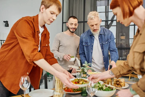 Gay hombre setting familia cena cerca padres y novio en cocina - foto de stock