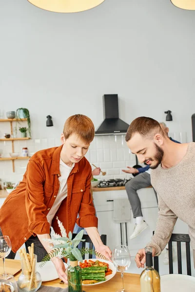 Rossa gay uomo servizio grigliato asparagi vicino fidanzato in moderno cucina — Foto stock