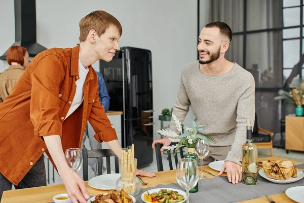 Happy gay couple looking at each other near prepared supper in modern kitchen — Stock Photo