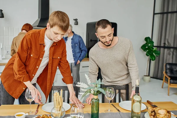 Young gay couple setting family supper near parents in kitchen — Stock Photo