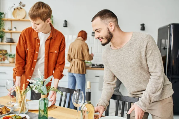 Joven gay pareja setting familia cena cerca padres en borrosa fondo en cocina - foto de stock