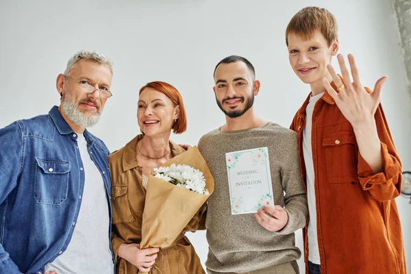 Happy gay man showing wedding ring near parents with flowers and boyfriend with wedding invitation — Stock Photo