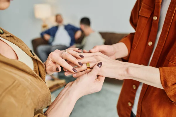 Vista parcial de la mujer tocando las manos del hombre gay con anillo de bodas en casa - foto de stock