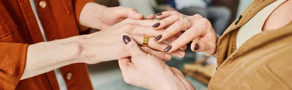 Vista recortada de la madre tocando la mano del hijo comprometido con anillo de boda, bandera - foto de stock