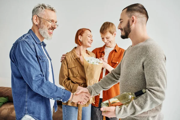 Pleased father shaking hands with gay man near mother and son with flowers at home — Stock Photo