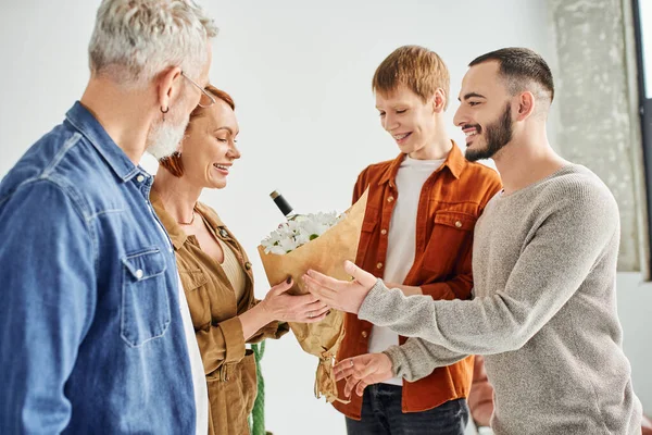 Smiling gay couple giving flowers to happy parents at home — Stock Photo