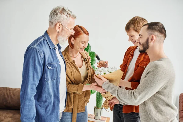 Young and happy gay couple giving bouquet to pleased parents at home — Stock Photo