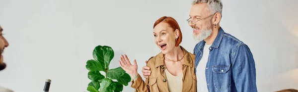 Amazed woman with happy husband showing wow gesture while meeting blurred son at home, banner — Stock Photo