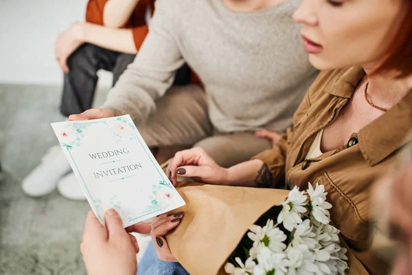 Cropped view of shocked woman with flowers looking at wedding invitation near young gay couple — Stock Photo