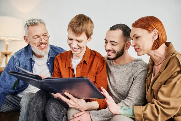 Smiling gay partners with parents looking at family photo album in living room — Stock Photo