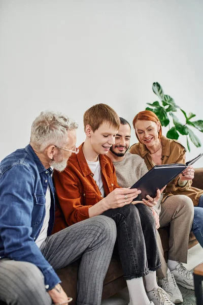 Jeune couple gay et heureux parents assis sur le canapé dans le salon et en regardant album photo — Photo de stock