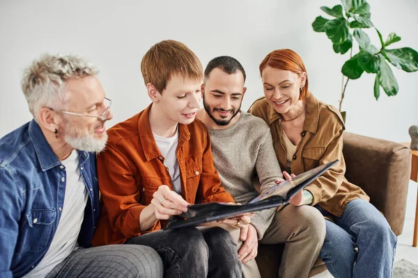 Redhead gay man looking at photo album together with boyfriend and joyful parents — Stock Photo