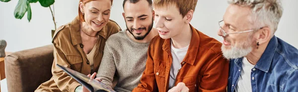 Cheerful gay couple with parents looking at family photo album at home, banner — Stock Photo